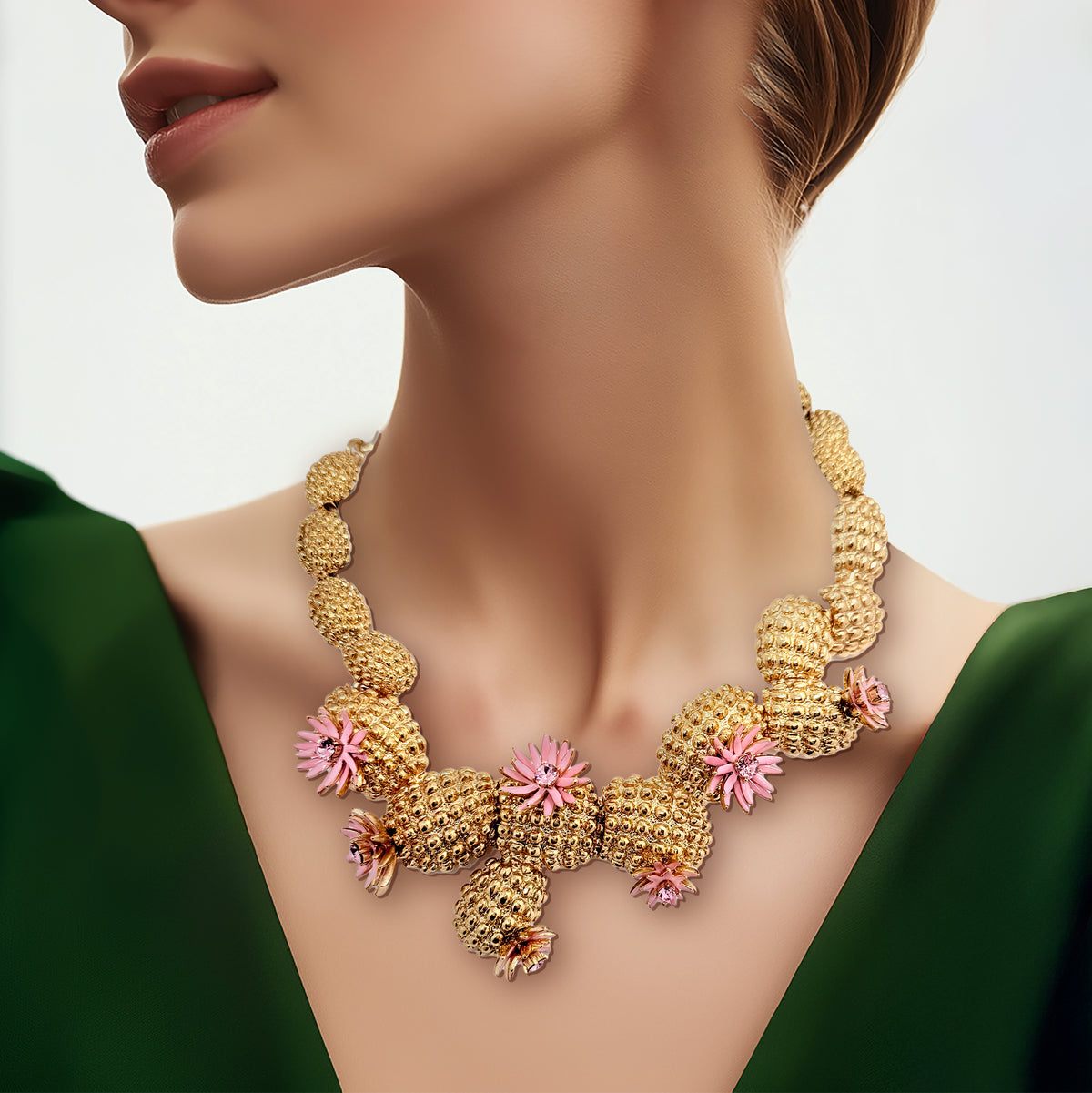 Close-up of Oscar de la Renta cactus blossom necklace in antique gold with sculpted cacti sections and pink enamel flowers, worn with a deep green dress.