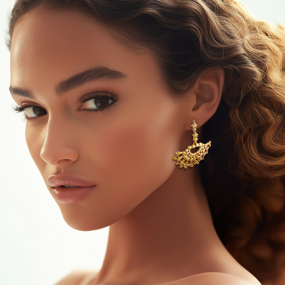 Model wearing Oscar de la Renta gold fan earrings, displaying the luminous design and starry details against a soft, elegant look.