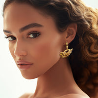 Model wearing Oscar de la Renta gold fan earrings, displaying the luminous design and starry details against a soft, elegant look.