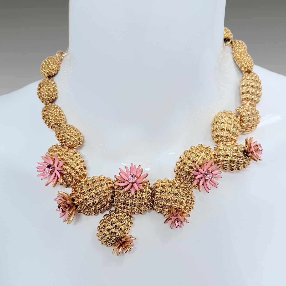  Close-up of the Oscar de la Renta necklace on a display bust, showing detailed cacti texture and vibrant pink enamel flowers.