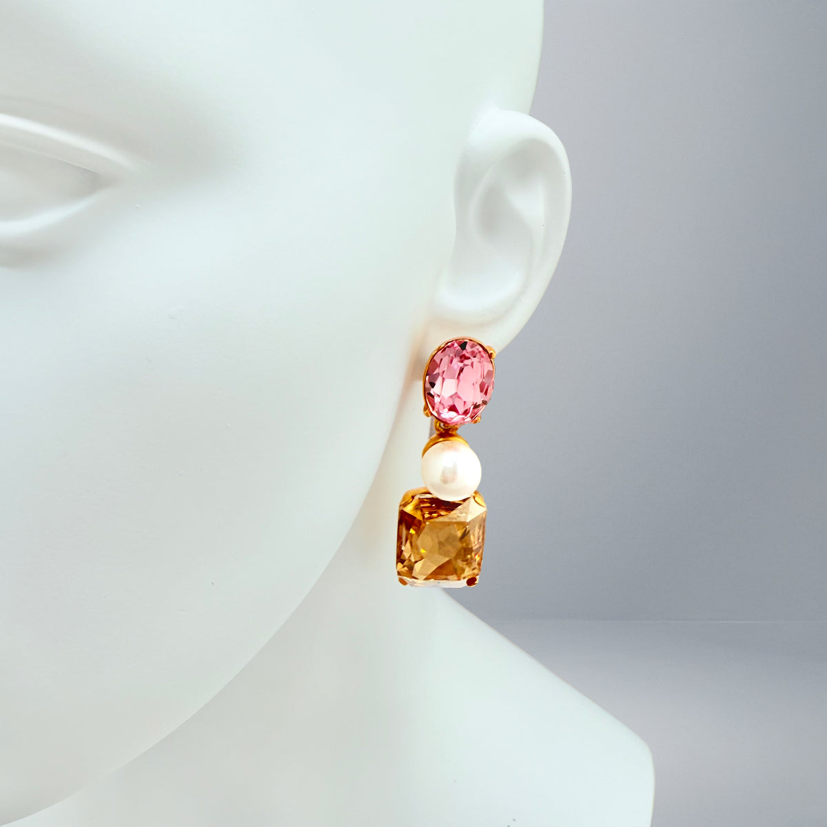 Close-up of Oscar de la Renta asymmetrical clip-on earrings featuring rose and light rose Austrian crystals with pearl accents, set in antique gold plating