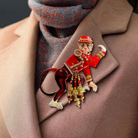 Close-up of a Lunch at The Ritz Organ Grinder Monkey Pin worn on a tan jacket, showing intricate red enamel detailing and dangling Swarovski crystal accents